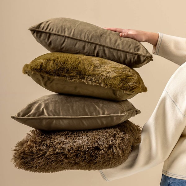 Stapel aus vier Dekokissen mit Bezügen aus Samt und Kunstfell, die von einer Person gehalten werden.