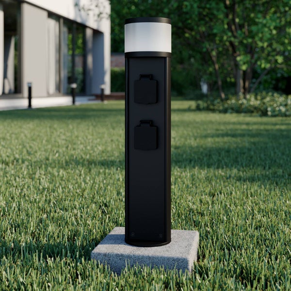 Schwarze Außensteckdosensäule mit integrierter LED-Leuchte und zwei Steckdosen auf einer Rasenfläche im Garten.