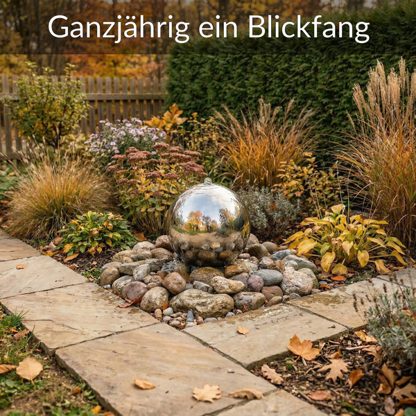 Edelstahl-Kugelbrunnen auf einem Bett aus Natursteinen in einem herbstlichen Garten mit Steinplatten und Zierpflanzen.