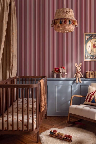 Ein Kinderzimmer mit gestreifter Tapete, einem hölzernen Kinderbett, einem Schaukelstuhl und Zirkus-Dekorationselementen.
