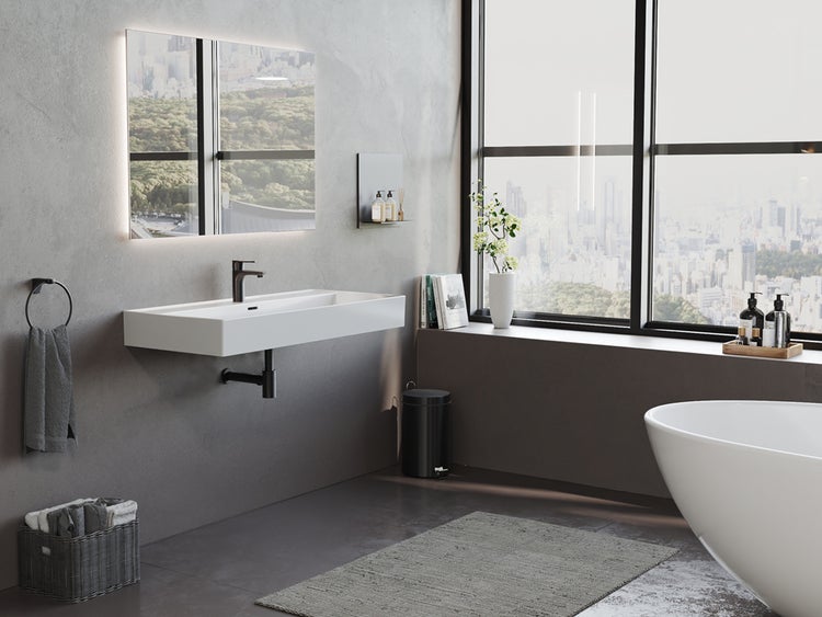 Modernes Bad mit weißem Waschtisch, schwarzer Armatur, beleuchtetem Spiegel und freistehender Wanne vor grauen Wänden in Betonoptik.