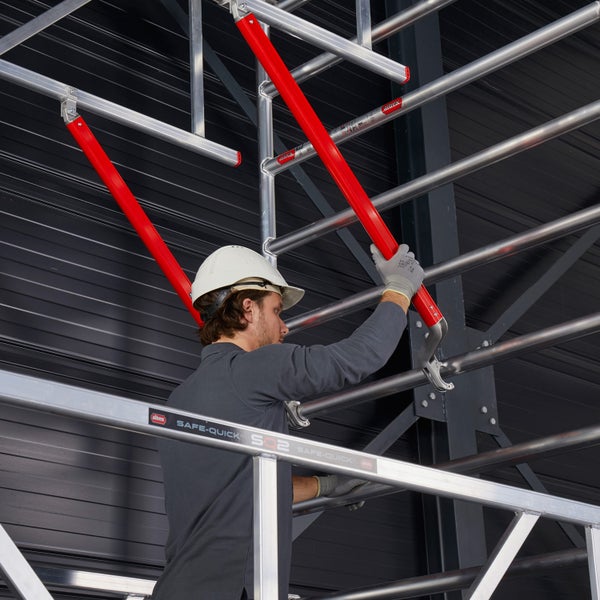 Mann mit Schutzhelm montiert ein Baugerüst aus Aluminium.
