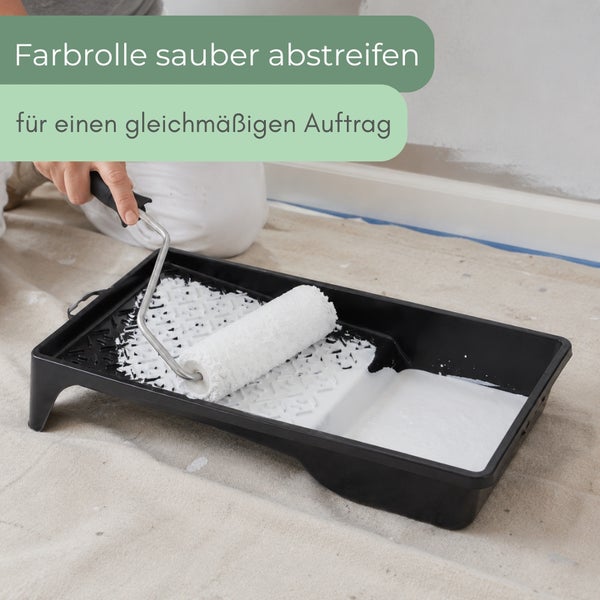 Eine Hand streift eine Farbrolle in einer Farbwanne ab, um einen gleichmäßigen Farbauftrag zu erzielen.