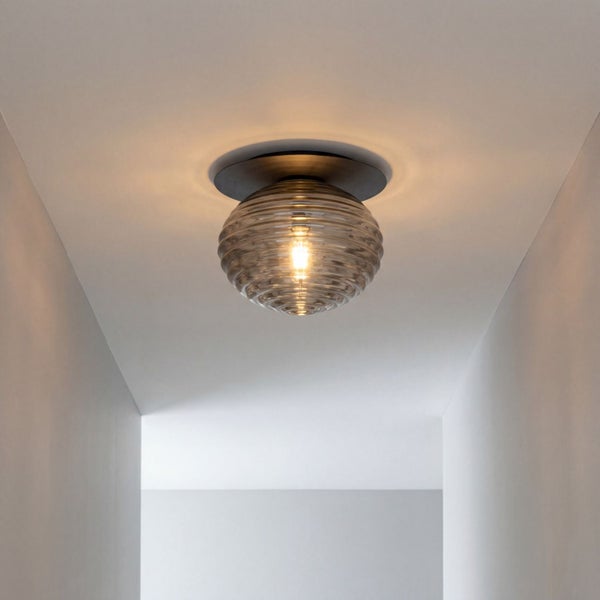 Deckenleuchte mit geriffeltem Glasschirm und schwarzem Metallsockel, montiert in einem hellen, minimalistischen Flur.