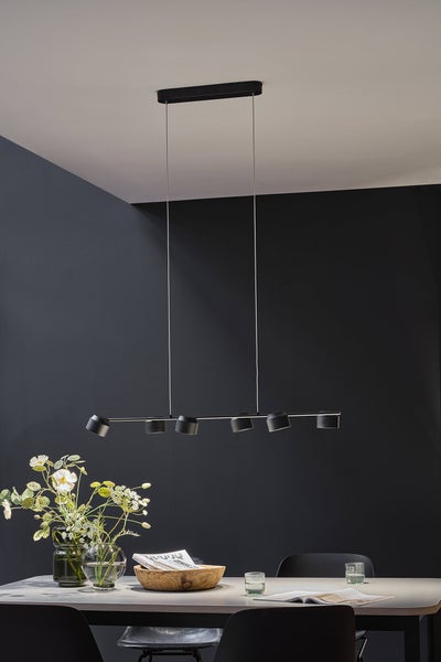 Moderne schwarze LED-Pendelleuchte mit sechs verstellbaren Spots über einem Esstisch in einem minimalistisch eingerichteten Raum.
