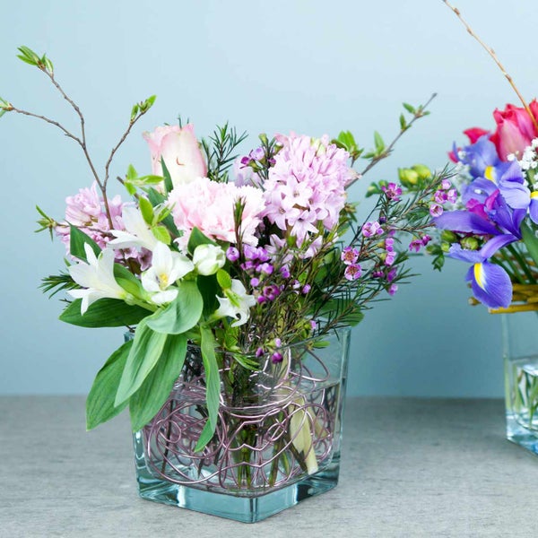 Mischstrauß mit Frühlingsblumen wie Hyazinthen und Rosen in einer quadratischen Glasvase.