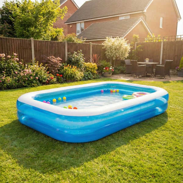 Rechteckiges aufblasbares Familienplanschbecken auf einem Gartenrasen mit verstreuten Spielbällen und Schwimmringen.