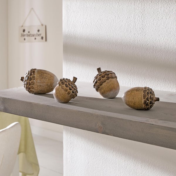 Vier dekorative Eicheln aus Kunststoff als herbstliche Tischdekoration auf einem Holzregal