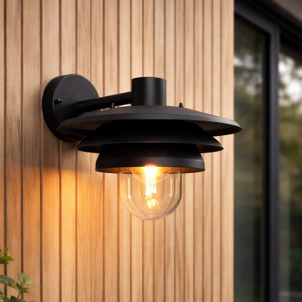 Moderne Außenwandleuchte aus schwarzem Metall mit dreistufigem Schirm und Glaskolben an einer Holzfassade.