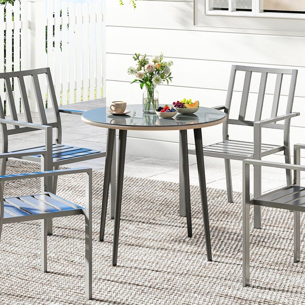 Moderner runder Gartentisch mit Glasplatte und vier Gartenstühle aus Metall auf einer hellen, organisierten Terrasse mit Teppich.