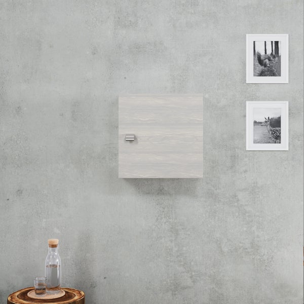 Quadratischer Hängeschrank in Holzoptik an einer Wand in Betonoptik, dekoriert mit zwei Bildern und einer Karaffe auf einem Beistelltisch.