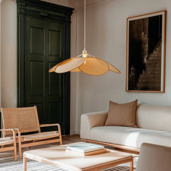 Pendelleuchte mit fächerförmigen Schirmen aus Geflecht in einem hellen Wohnzimmer mit Sofa, Holztisch und dunkelgrüner Tür.