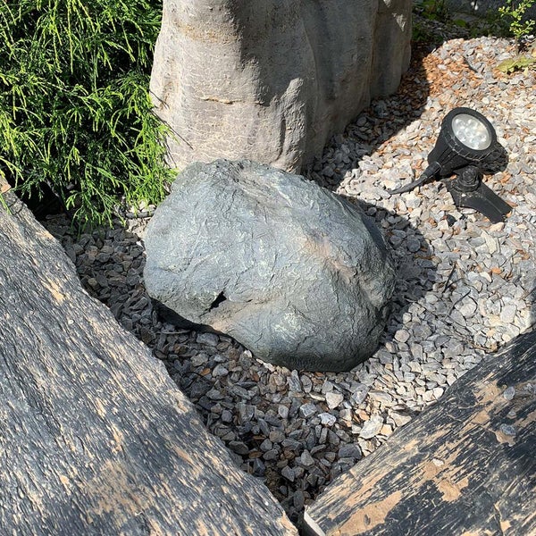 Strukturierter Gartenbereich mit künstlichem Felsstein auf Zierkies, Gartenstrahler, Holzschwellen und grünen Pflanzen.