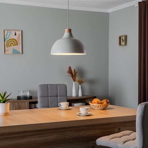 Graue Pendelleuchte mit Holzelement über einem Holztisch in einem hellen, modern eingerichteten Esszimmer mit grauen Polsterstühlen.