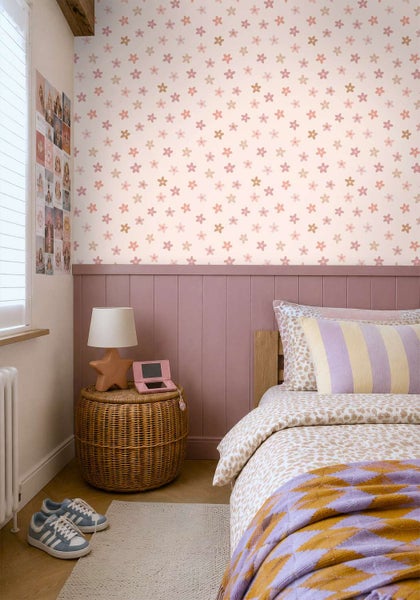 Kinderschlafzimmer mit geblümter Vliestapete, Holzpaneelen an der Wand, Korb-Nachtisch, Lampe und gemustertem Bettzeug.