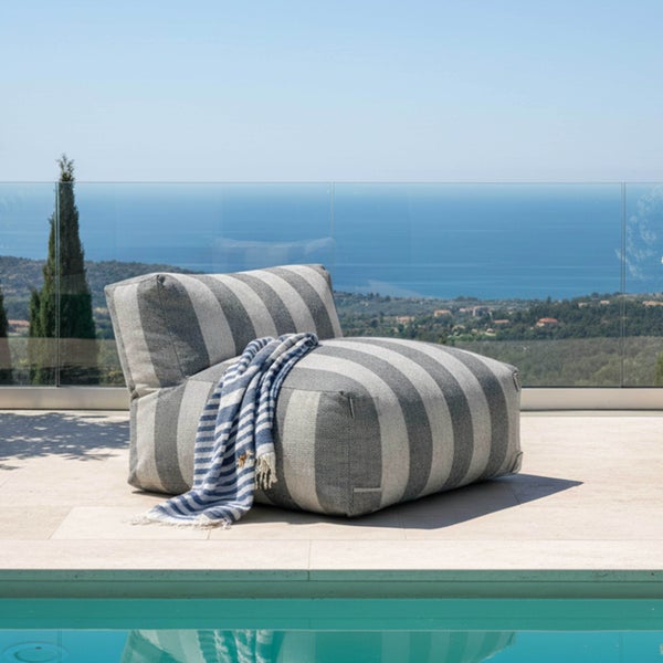 Gestreifter Outdoor-Sitzsack in Grau und Weiß mit blau-weißer Decke auf einer hellen Terrasse am Pool mit Meerblick.