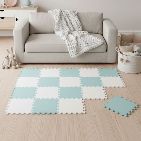 Puzzlematte aus Schaumstoff mit Schachbrettmuster auf hellem Boden im Wohnzimmer vor einem Sofa mit Decke und Spielzeug.