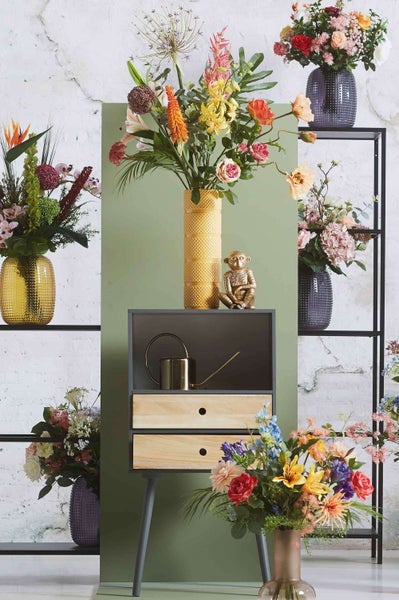 Künstliche Monstera-Kletterpflanze mit grünen, geschlitzten Blättern und braunen Luftwurzeln.