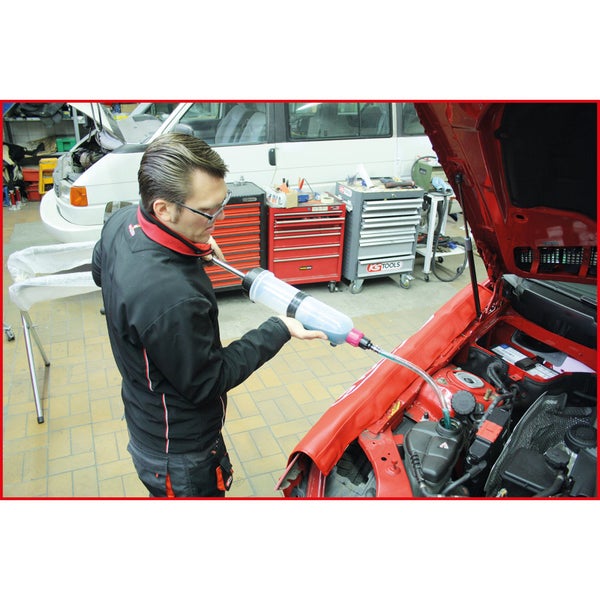 Ein Mann befüllt mit einer Ölabsaugpumpe Kühlflüssigkeit in ein rotes Auto.