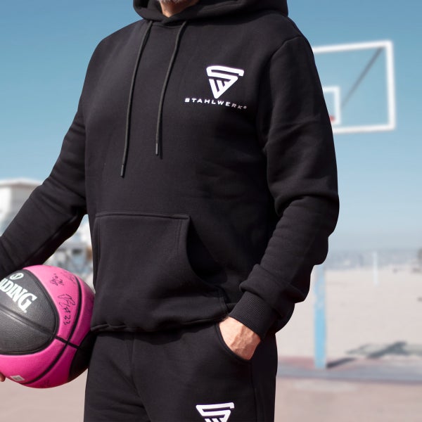 Person mit schwarzem Kapuzenpullover und Trainingshose mit Stahlwerk Logo und Basketball