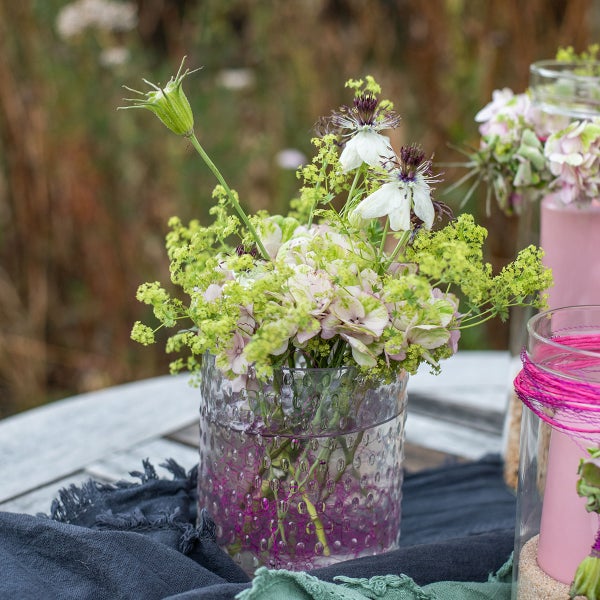 Strukturierte Glasvase mit einem Blumenstrauß auf einem rustikalen Holztisch im Freien.