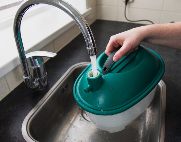 Eine Person befüllt einen Kunststoff Gießkannenbehälter unter einem Wasserhahn an einer Küchenspüle.