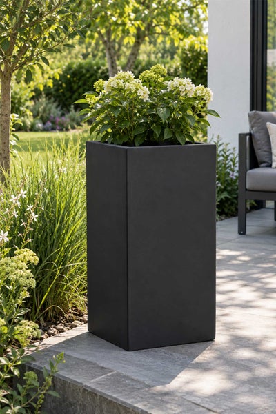 Hoher quadratischer Pflanzkübel aus Kunststoff auf einer Terrasse mit Blumenbepflanzung im Garten