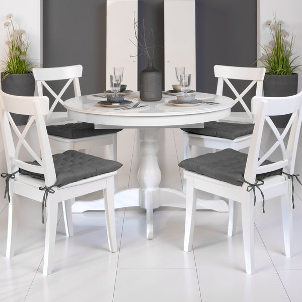 Weißer runder Esstisch mit vier Stühlen und grauen Sitzkissen in einem hellen Raum.