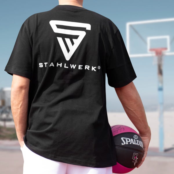 Mann mit schwarzem T-Shirt mit Stahlwerk Logo hält einen Spalding Basketball