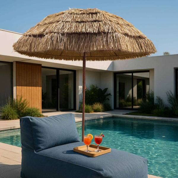 Sonnenschirm in Strohoptik neben einer blauen Gartenliege an einem Swimmingpool auf einer modernen Terrasse.