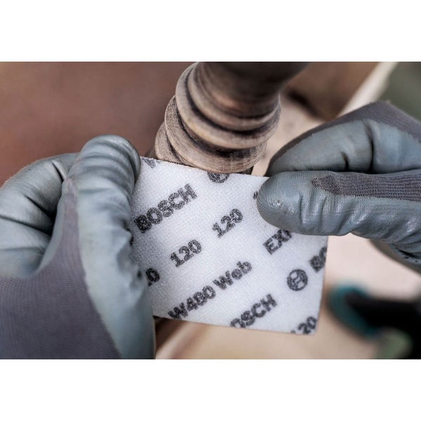 Eine Person schleift mit einem Schleifpapier der Körnung 120 ein Holzobjekt ab.