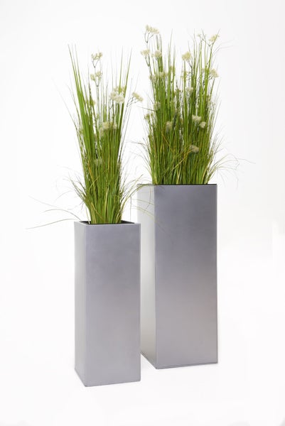 Zwei silberne Pflanzsäulen in verschiedenen Größen mit künstlichem Gras und kleinen weißen Blüten.