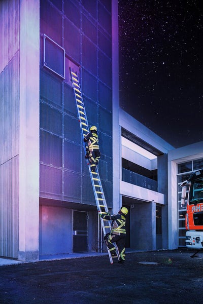 Feuerwehrleute steigen bei Nacht mit einer Leiter an einem Gebäude hoch