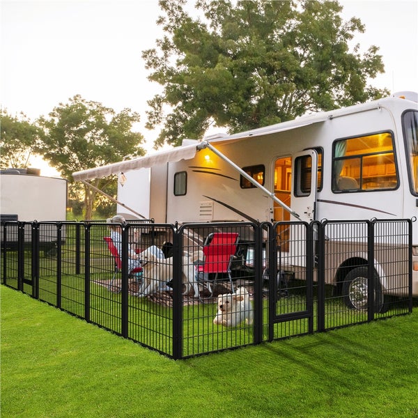 Szene mit einem schwarzen Metall-Hundezwinger, der auf einer grünen Wiese vor einem Wohnmobil steht.