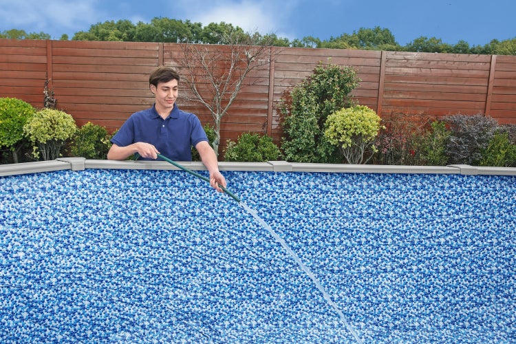 Ein Mann befüllt einen Aufstellpool mit Mosaik-Poolfolie mit einem Gartenschlauch in einem Garten mit einem Holzzaun.