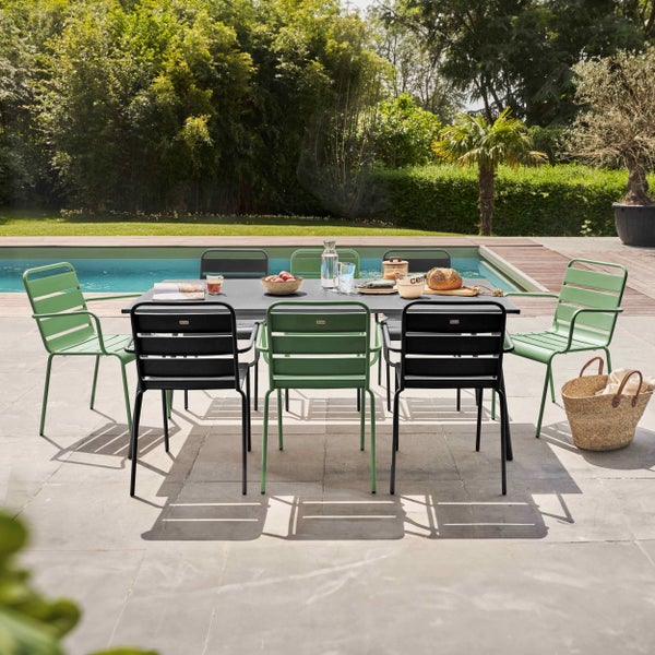 Modernes Garten-Essset aus Metall auf einer hellen Fliesenterrasse am Pool, bestehend aus einem dunklen Tisch und Stühlen in Grün und Schwarz.