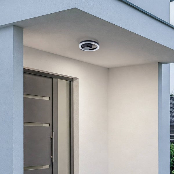 Moderne ringförmige LED Außen-Deckenleuchte, montiert unter einem Dachüberstand über einer grauen Haustür.