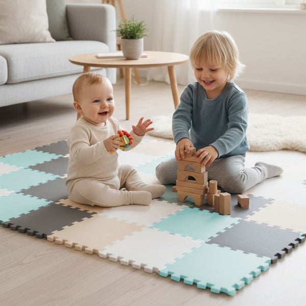 Zwei kleine Kinder spielen auf einer bunten Schaumstoff-Puzzlematte in einem hellen Wohnzimmer.