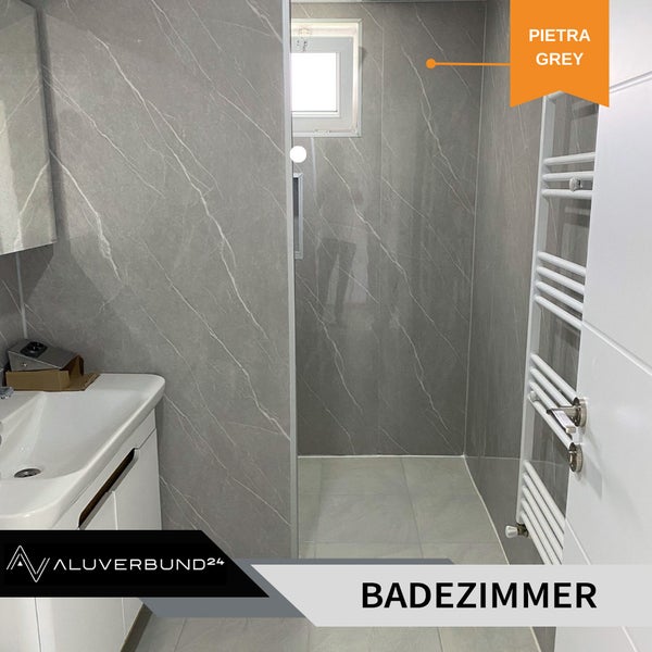 Badezimmer mit Waschbecken, Heizkörper und Duschbereich mit grauen Wandpaneelen in Marmoroptik.