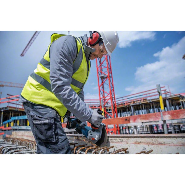 Bauarbeiter trennt Metallstäbe in Beton mit einem Winkelschleifer auf einer Baustelle. Er trägt Helm und Gehörschutz.