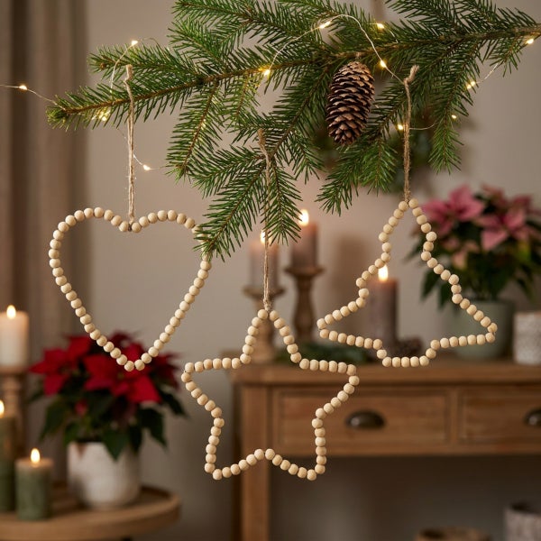 Drei hängende Weihnachtsanhänger aus Holzperlen in Herz Stern und Tannenbaum Form dekoriert an einem Tannenbaumzweig mit Lichterkette