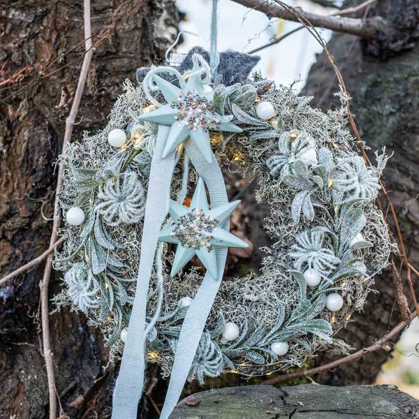 Dekorativer Türkranz mit Sternen, Schleife, Kugeln und Lichtern zur Weihnachtszeit.