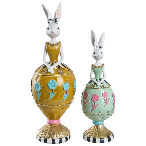 Zwei unterschiedlich große Osterhasen-Figuren in gelben und grünen eiförmigen Kleidern mit Blumenmustern auf gestreiften Sockeln.