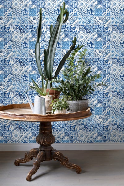Dekorative Zimmerpflanzen auf einem Holztisch vor einer Wand mit Fliesenmuster.
