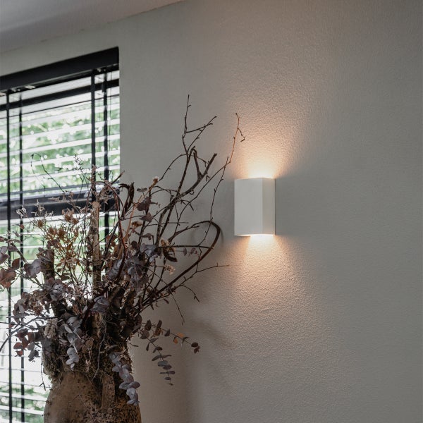 Weiße Wandleuchte neben einer Vase mit Dekoration an der Wand