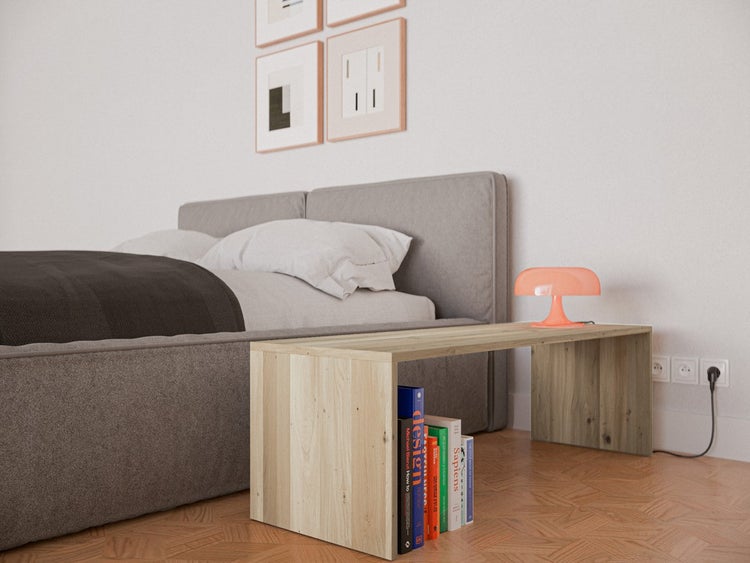 Moderne Schlafzimmerszene mit einer niedrigen Holzbank als Nachttisch neben einem grau gepolsterten Bett auf Parkettboden.