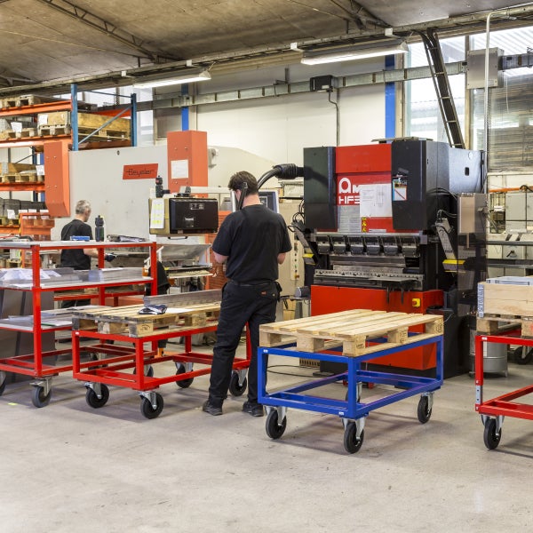 Innenaufnahme einer Werkshalle mit Personen, Werkzeugmaschinen und Transportwagen