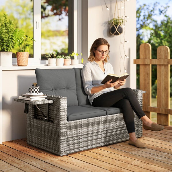 Zweisitzer Gartensofa aus Polyrattan in Grau mit Sitzkissen und ausklappbarem Seitentisch auf einer sonnigen Terrasse.