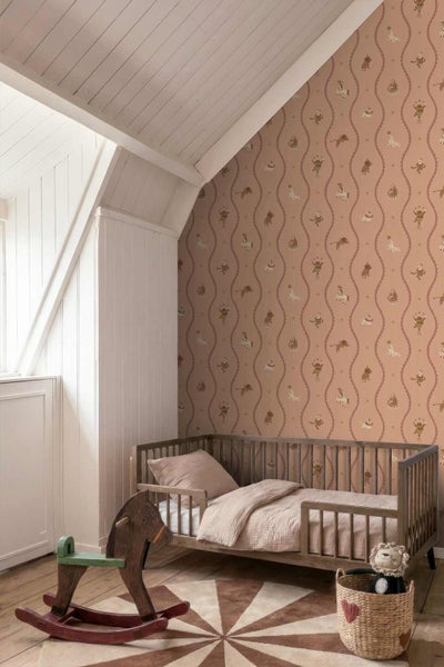 Kinderzimmer mit Vliestapete mit Zirkusmotiven, einem Kinderbett aus Holz, einem Schaukelpferd und einem Teppich unter einer Dachschräge.