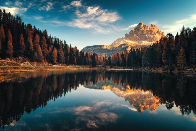 Landschaftsfotografie einer Berglandschaft mit See, Nadelwald und Berggipfel bei Sonnenlicht.